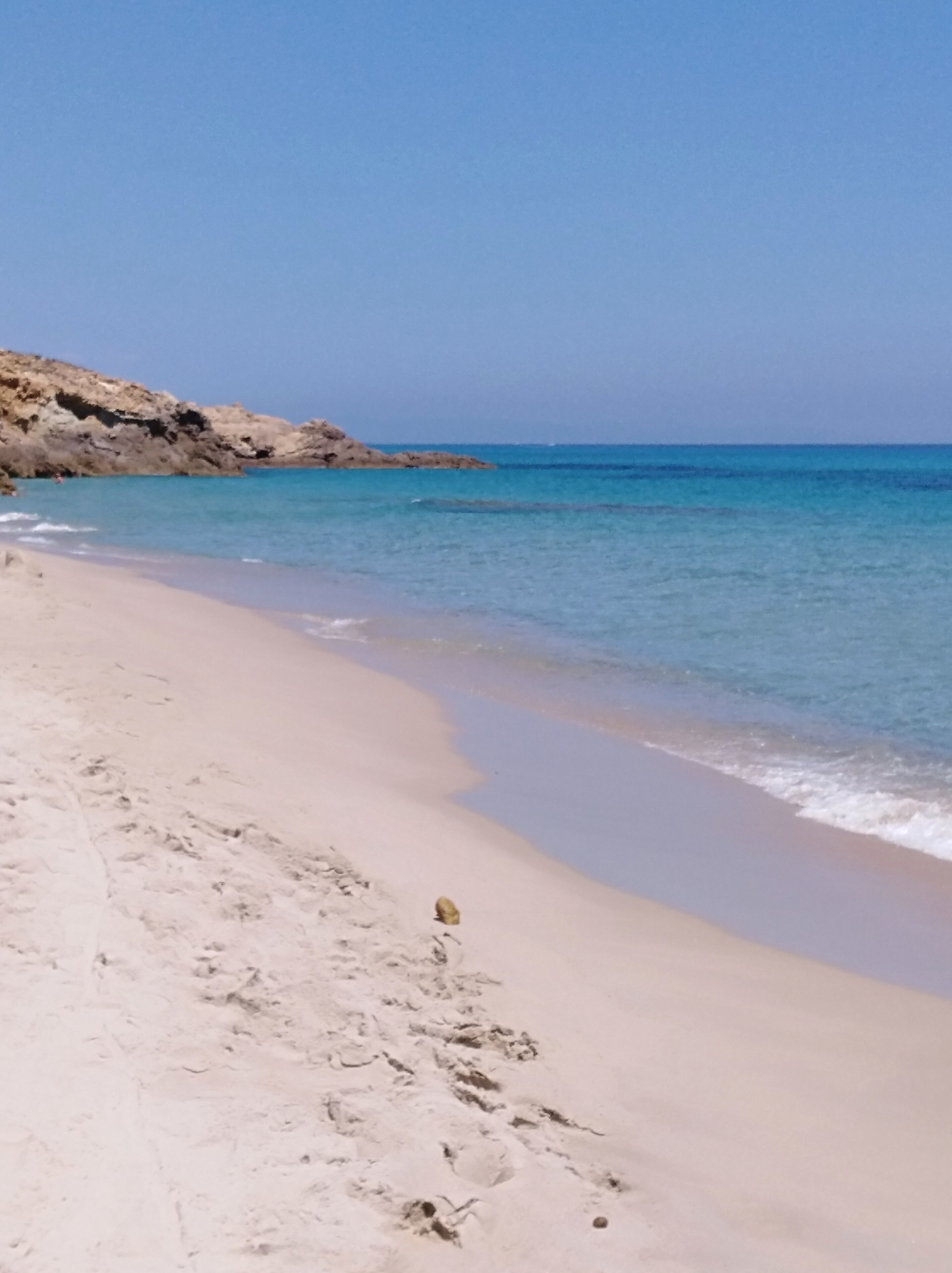A beach with clear blue water, sandy shore, and rocky cliffs.