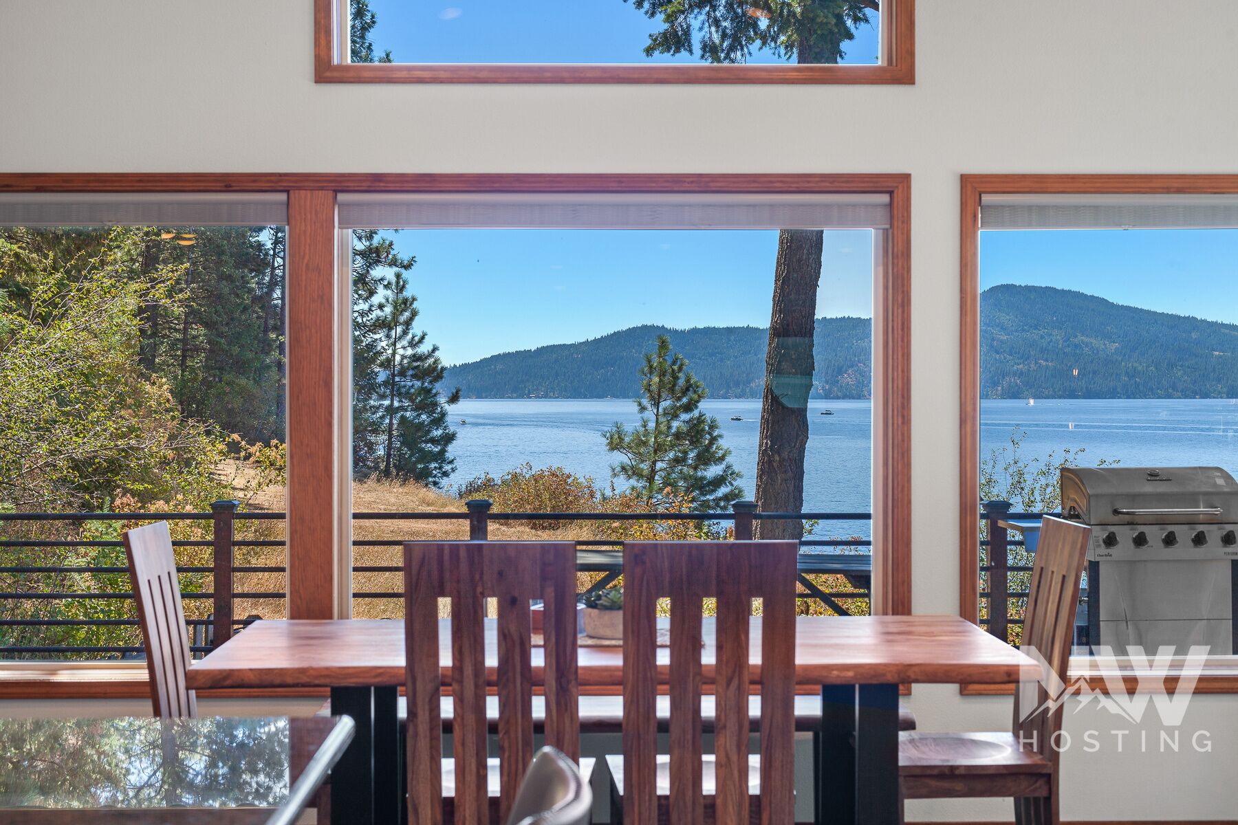 A dining area with a view of a lake and mountains, wooden furniture, and a grill.
