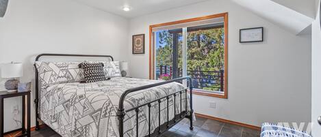 Un dormitorio con cama, mesita de noche, ventana con vista a árboles e iluminación empotrada en el techo.