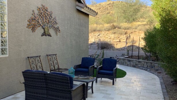 Une terrasse extérieure aménagée avec des meubles en osier et agrémentée d’une œuvre d’art décorative fixée au mur.