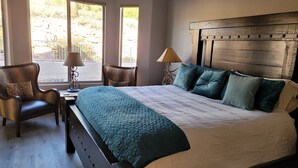 Une chambre avec un grand lit, une chaise, une lampe et une vue sur l’extérieur par la fenêtre.