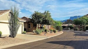 Une rue résidentielle bordée de maisons, un ciel dégagé et des montagnes à l’horizon.