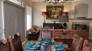 Une salle à manger avec une table en bois dressée pour le repas, un lustre et une cheminée en arrière-plan.