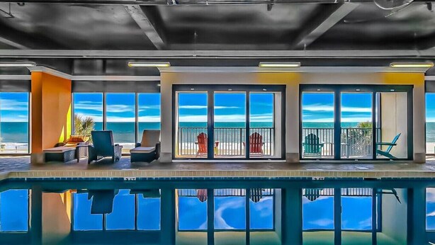 Un espace piscine avec vue sur l’océan, de grandes portes-fenêtres coulissantes et un coin salon extérieur.