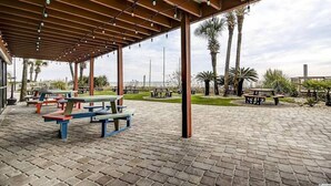 Un espace extérieur couvert, aménagé en patio, avec des tables de pique-nique et des palmiers.