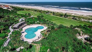 An aerial view of a resort with a swimming pool, beachfront, and lush greenery.