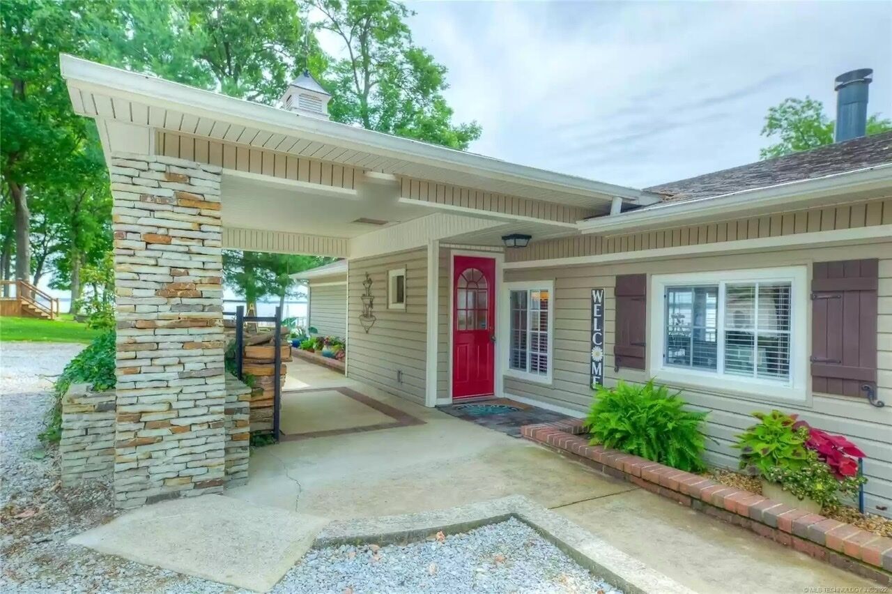 Une maison à deux étages, avec un pilier en pierre, une porte rouge et une pancarte indiquant « Bienvenue ».