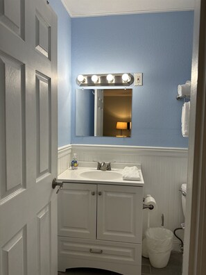 Une salle de bain avec un meuble-lavabo blanc, un évier, un miroir avec éclairage, un porte-serviettes et des toilettes.