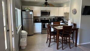 Una cocina moderna con armarios blancos, electrodomésticos de acero inoxidable y una zona de comedor con sillas de madera.