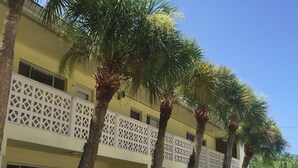 Un edificio de varios pisos con fachada amarilla, balcones de celosía blanca y palmeras.