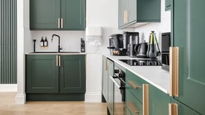 A modern kitchen with green cabinets, a white countertop, and stainless steel appliances. - Be More Elizabeth! (Greater London)