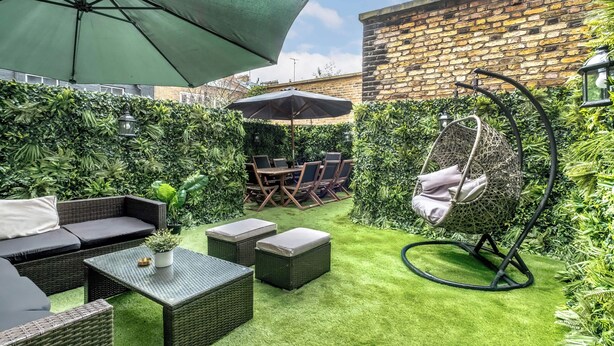 A patio with wicker furniture, a hanging chair, and a table with a potted plant. - Be More Elizabeth! (Greater London)