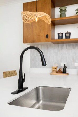 Cozinha moderna com pia de aço inoxidável, torneira preta e luminária de fibra natural.
