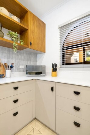 Une cuisine moderne avec des meubles en bois, un four à micro-ondes et une fenêtre équipée de stores.