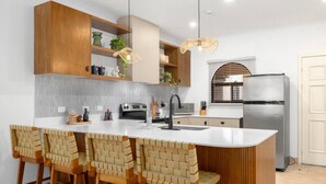 A modern kitchen with a central island, bar stools, wooden cabinets, and a stainless steel refrigerator. - SR9: Luxury Condo Across the Street from Beach (Tamarindo)