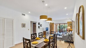 A dining area with a long wooden table, multiple chairs, and hanging pendant lights. - SR9: Luxury Condo Across the Street from Beach (Tamarindo)