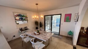 Un comedor con una mesa de mármol, sillas blancas, una araña y un gran ventanal corredizo que da a un patio exterior.