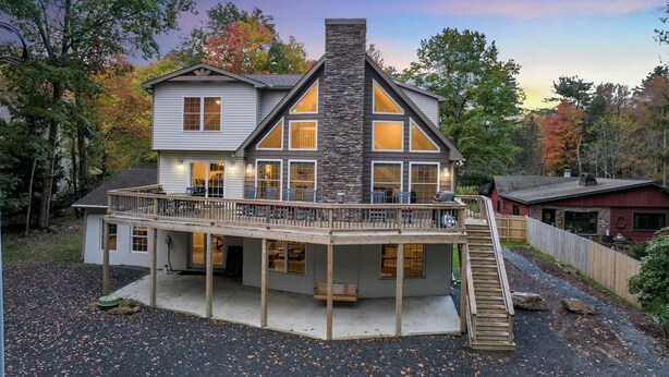 Une maison à deux étages avec une cheminée en pierre, de grandes fenêtres et une terrasse en bois.