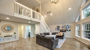 Un salon spacieux avec un grand canapé d’angle, un escalier et une vue sur l’extérieur grâce à de grandes fenêtres.