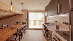 A modern kitchen with wooden beams, a dining table, chairs, and stainless steel appliances. - Le Chenaillet, duplex at the foot of the slopes and spa (Montgenèvre)