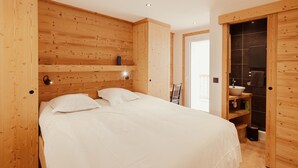 A bedroom with a wooden headboard, a bed with white bedding, a nightstand, and a small shelf with a lamp. - Le Chenaillet, duplex at the foot of the slopes and spa (Montgenèvre)