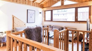 A wooden interior with a staircase, a sofa, a bear-themed artwork, and a large window. - Le Chenaillet, duplex at the foot of the slopes and spa (Montgenèvre)