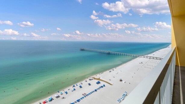 Een strand met een pier die zich uitstrekt over de oceaan, wit zand en helderblauw water.