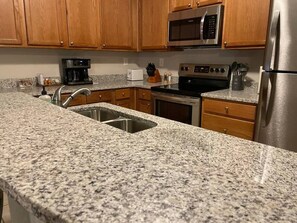 A kitchen with granite countertops, stainless steel appliances, wooden cabinets, and a double sink.