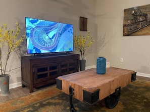 A living room with a TV on a wooden cabinet, a coffee table with wheels, and two potted plants.