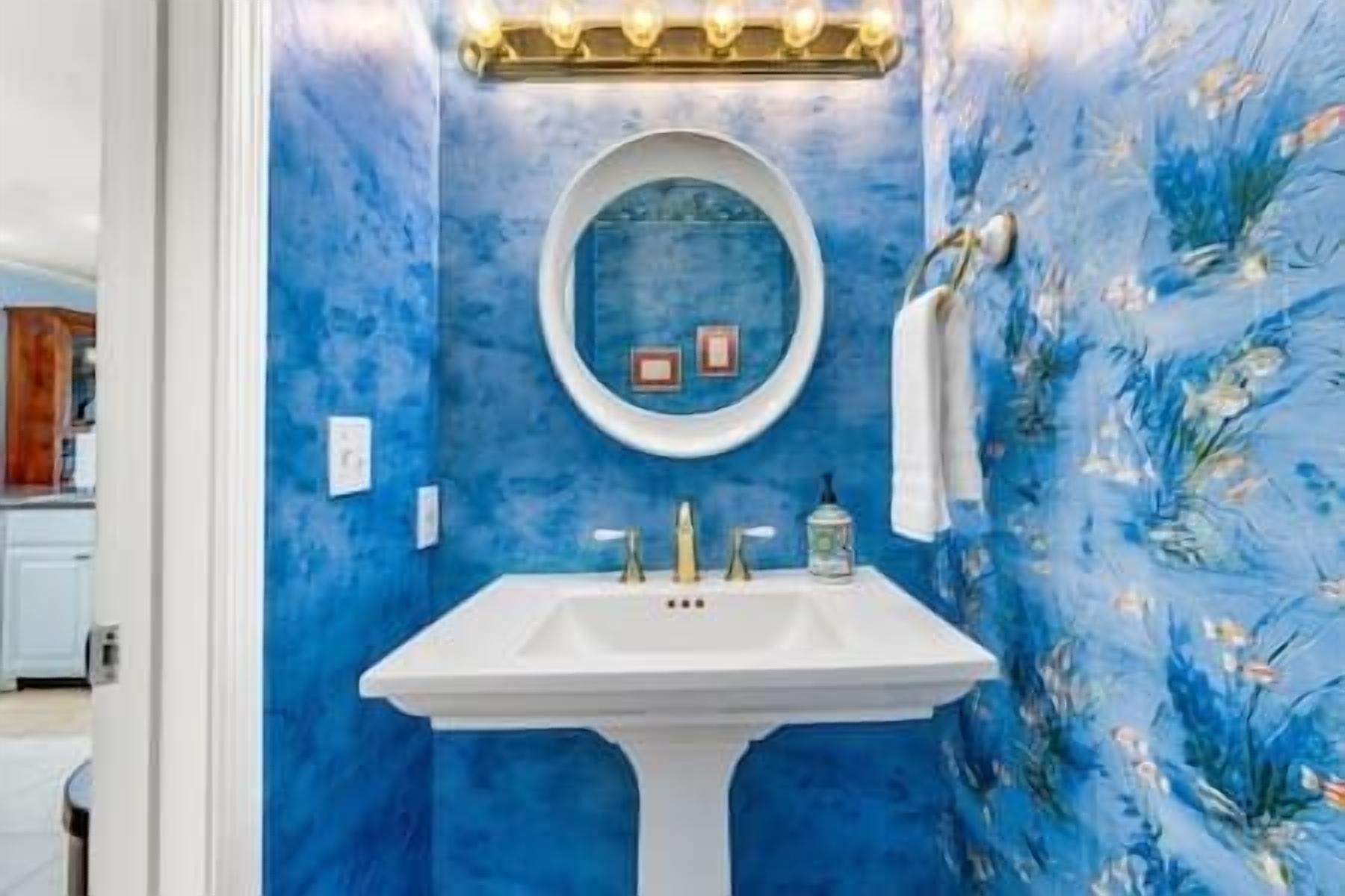 Une salle de bain avec un lavabo blanc, un mur bleu et un miroir surmonté de lampes.