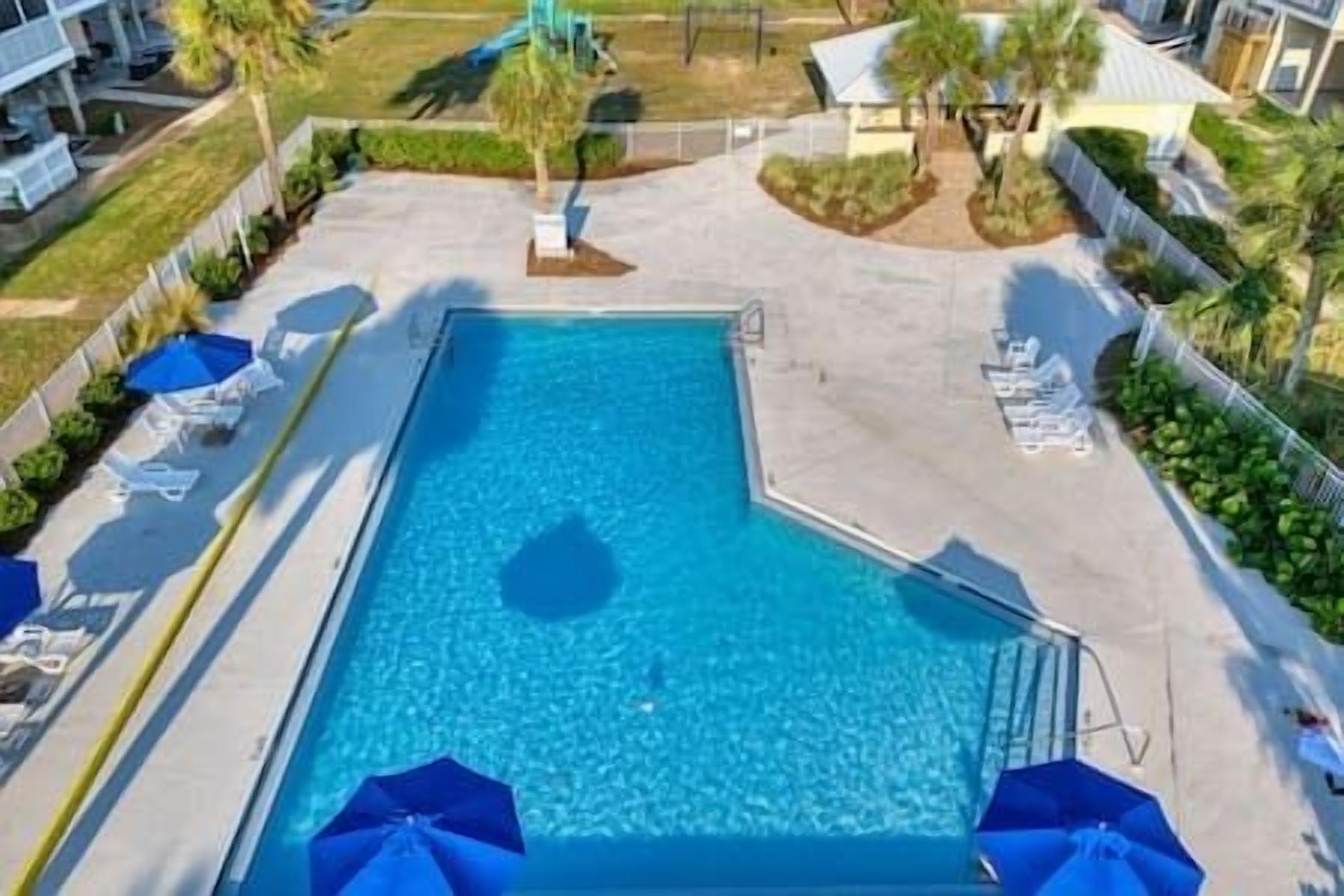 Une piscine rectangulaire à l’eau d’un bleu limpide, entourée d’une terrasse en béton. Des chaises longues et des parasols sont disposés le long du bord de la piscine.