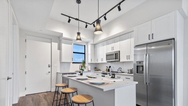 A modern kitchen with white cabinets, a stainless steel refrigerator, and a central island with stools.