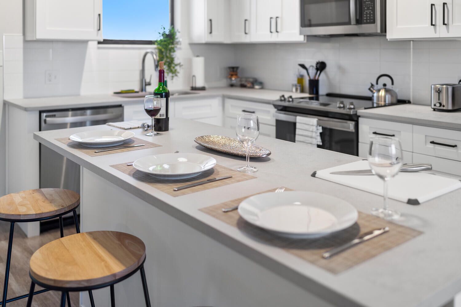 Une cuisine moderne avec des meubles blancs, un îlot central aménagé en coin repas et une vue sur l’extérieur.