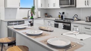 A modern kitchen with white cabinetry, a central island with dining setup, and a view of the outdoors.