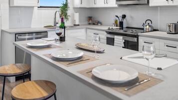Une cuisine moderne avec des meubles blancs, un îlot central aménagé en coin repas et une vue sur l’extérieur.