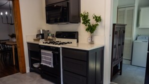 A compact kitchen with a stove, microwave, and a sink. There is a small dining area with a table and chairs.