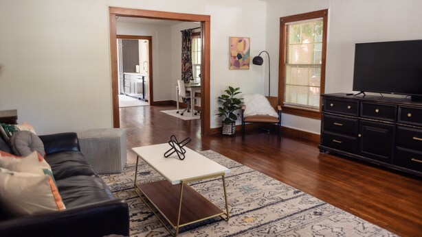 A living room with a black leather sofa, a white coffee table, a black TV stand, and a patterned rug.