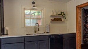 A kitchen with a built-in dishwasher, a window, and a shelf with bottles and plants.