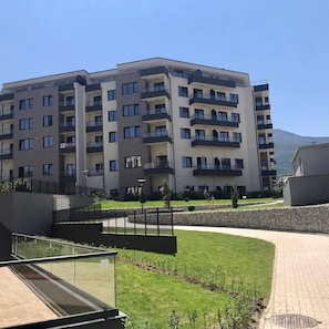 Un hôtel à plusieurs étages doté de balcons, d’un jardin aménagé et ayant une montagne en toile de fond.