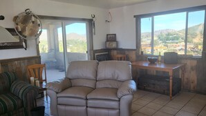 Una stanza con un divano in pelle color beige, un tavolo da pranzo in legno e un'ampia finestra che si affaccia su un paesaggio collinare.