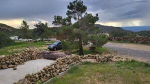 Paesaggio rurale con un muro in pietra, un SUV parcheggiato e una casa sullo sfondo.