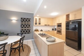 A modern kitchen with a central island, a dining area with chairs, and a light-colored backsplash.