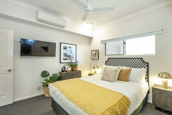 A bedroom with a bed, bedside tables, a TV, a window, and a ceiling fan.