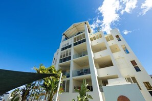 A multi-story hotel with balconies, a clear sky, and some greenery in the foreground. - Luxury City Escape – Stylish 3-Bedroom Apartment with Balcony & Rooftop Pool! (Cairns City)