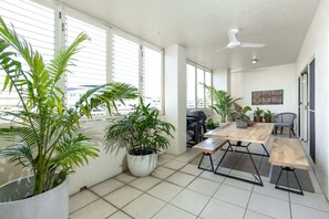 A spacious balcony with a wooden table and chairs, surrounded by potted plants. - Luxury City Escape – Stylish 3-Bedroom Apartment with Balcony & Rooftop Pool! (Cairns City)