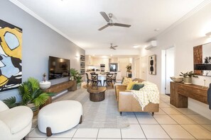 A modern living room with a sofa, coffee table, and a dining area with chairs and a table. - Luxury City Escape – Stylish 3-Bedroom Apartment with Balcony & Rooftop Pool! (Cairns City)