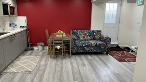 Ein kompakter Wohnraum mit Esstisch, farbenfroher Couch, Mikrowelle und einer roten Akzentwand.