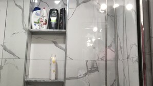 Eine Dusche mit Handbrause und Ablagefläche aus Glas für Toilettenartikel.