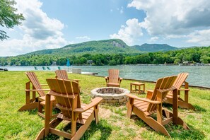 Un cadre idyllique au bord du lac, avec des fauteuils Adirondack et un foyer, le tout entouré d’une végétation luxuriante et de montagnes.