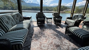 A room with a large window overlooking a lake and mountains, furnished with striped sofas and chairs.